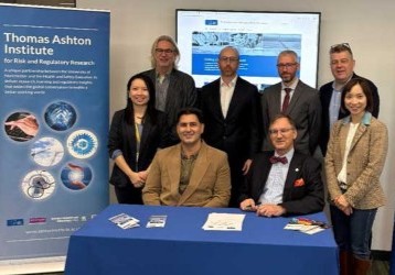 Eight people gathered for the launch of the Enhanced Learning from Incidents project, with Thomas Ashton Institute and EEMUA banners.