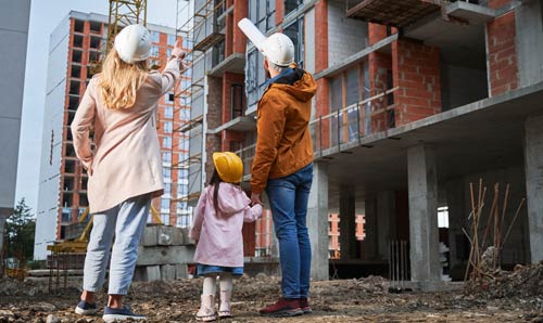 A back view of a man, woman and child wearing safety helmets, observing a construction site, emphasising workplace safety and teamwork in the construction industry