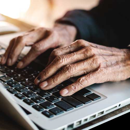Close-up of an elderly persons hands typing on a laptop keyboard