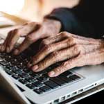 Close-up of an elderly persons hands typing on a laptop keyboard