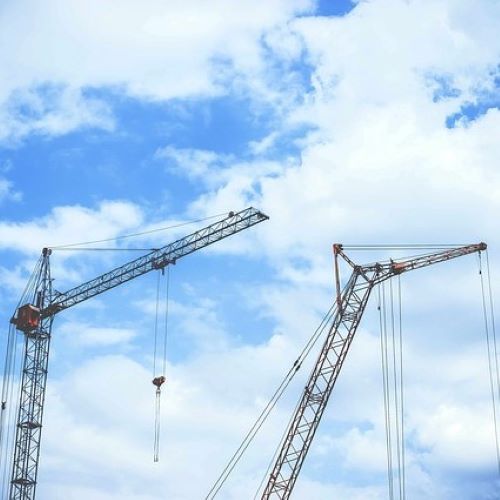 images shows tall construction cranes against a blue sky with clouds