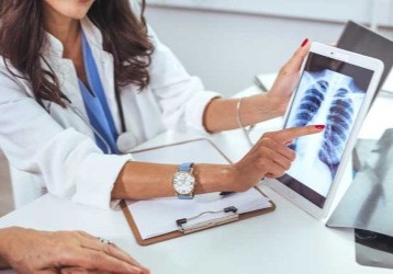 Healthcare professional pointing to a chest X-ray displayed on a tablet.